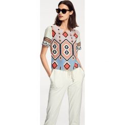 Koszulka w kolorze białym ze wzorem. T-shirty damskie marki Heine, z okrągłym kołnierzem, z krótkim rękawem. W wyprzedaży za 99.95 zł.
