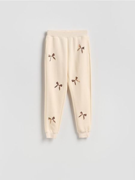 Spodnie dresowe z aplikacjami - złamana biel. Spodnie dresowe damskie Reserved, l, z aplikacjami, z bawełny. Za 99.99 zł.