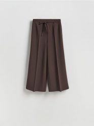 Szerokie spodnie z wiązaniem - ciemnobrązowy. Brązowe spodnie materiałowe damskie Reserved, bez wzorów, z tkaniny. Za 119.99 zł.