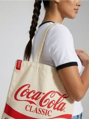 Materiałowa torba shopper z nadrukiem Coca Cola - kremowy. Białe torebki shopper damskie Sinsay, bez wzorów, z materiału, z nadrukiem, bez dodatków. Za 19.99 zł.